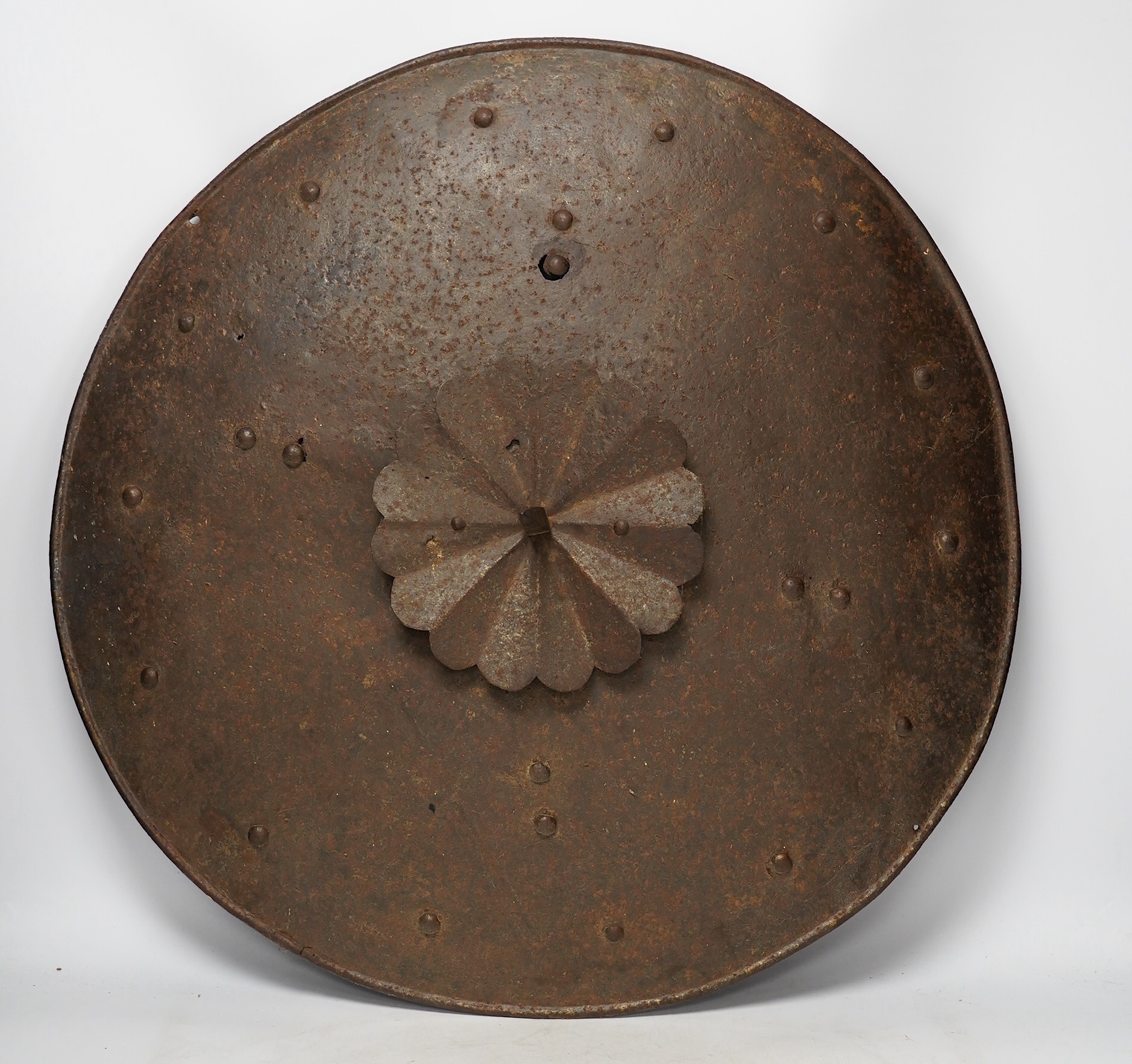 A 19th century iron shield with centre spike, formally part of a suit of armour, diameter 57.5cm. Condition - poor, surface rust and pitting overall.